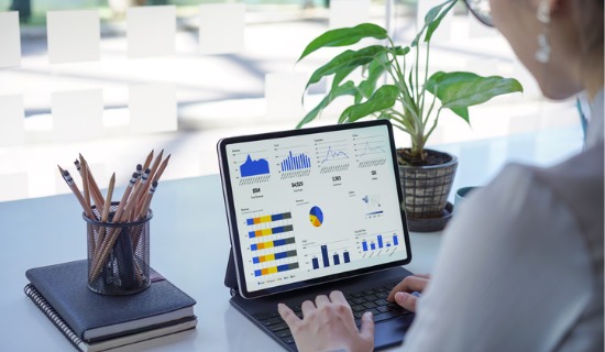 person at desk typing on tablet keyboard, screen shows financial graphs